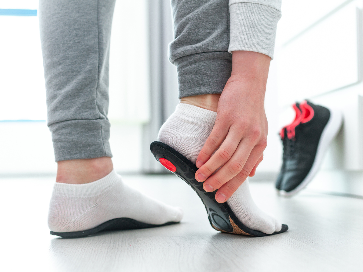 Person putting insole into socked foot next to sneaker. Grey sweatpants and white socks.