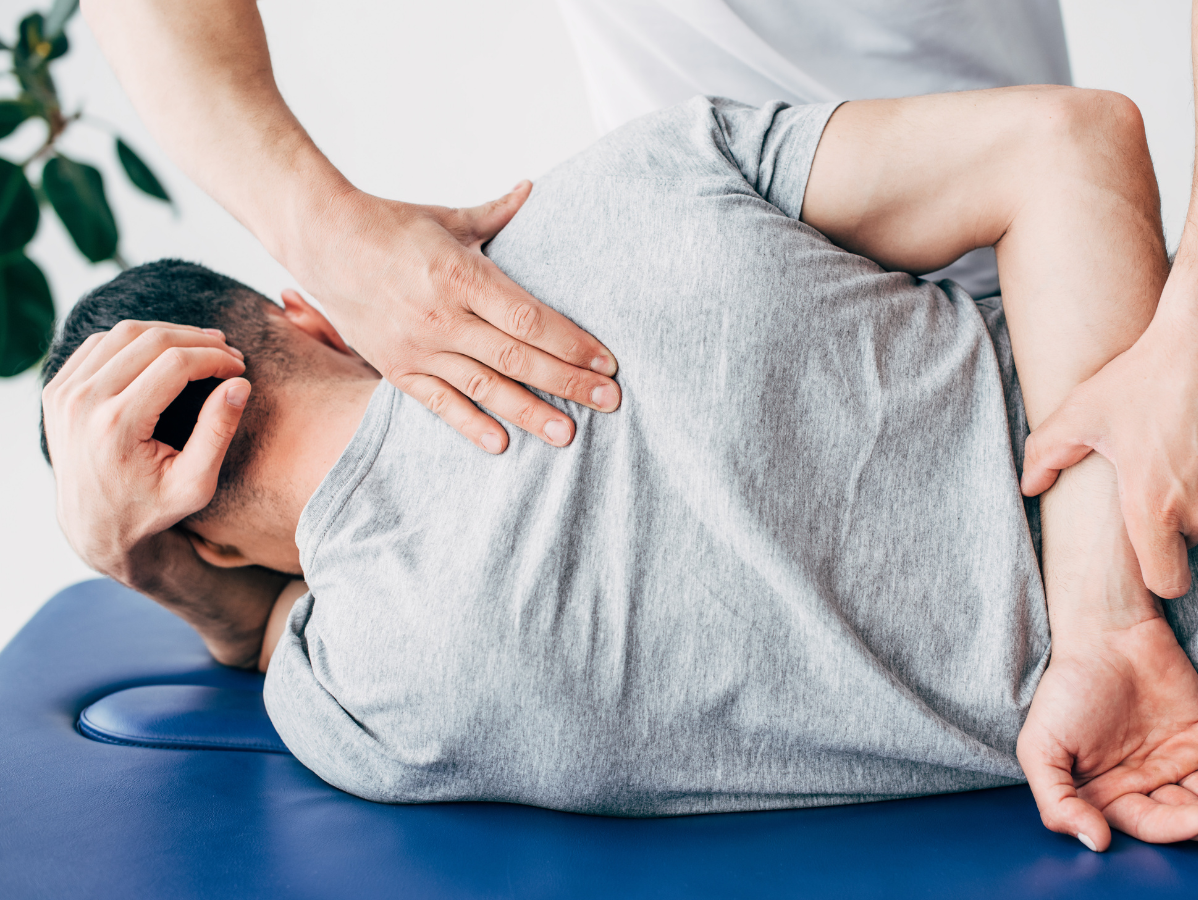 Chiropractor adjusting a man's back on a blue table; the man is lying on his side, face down.