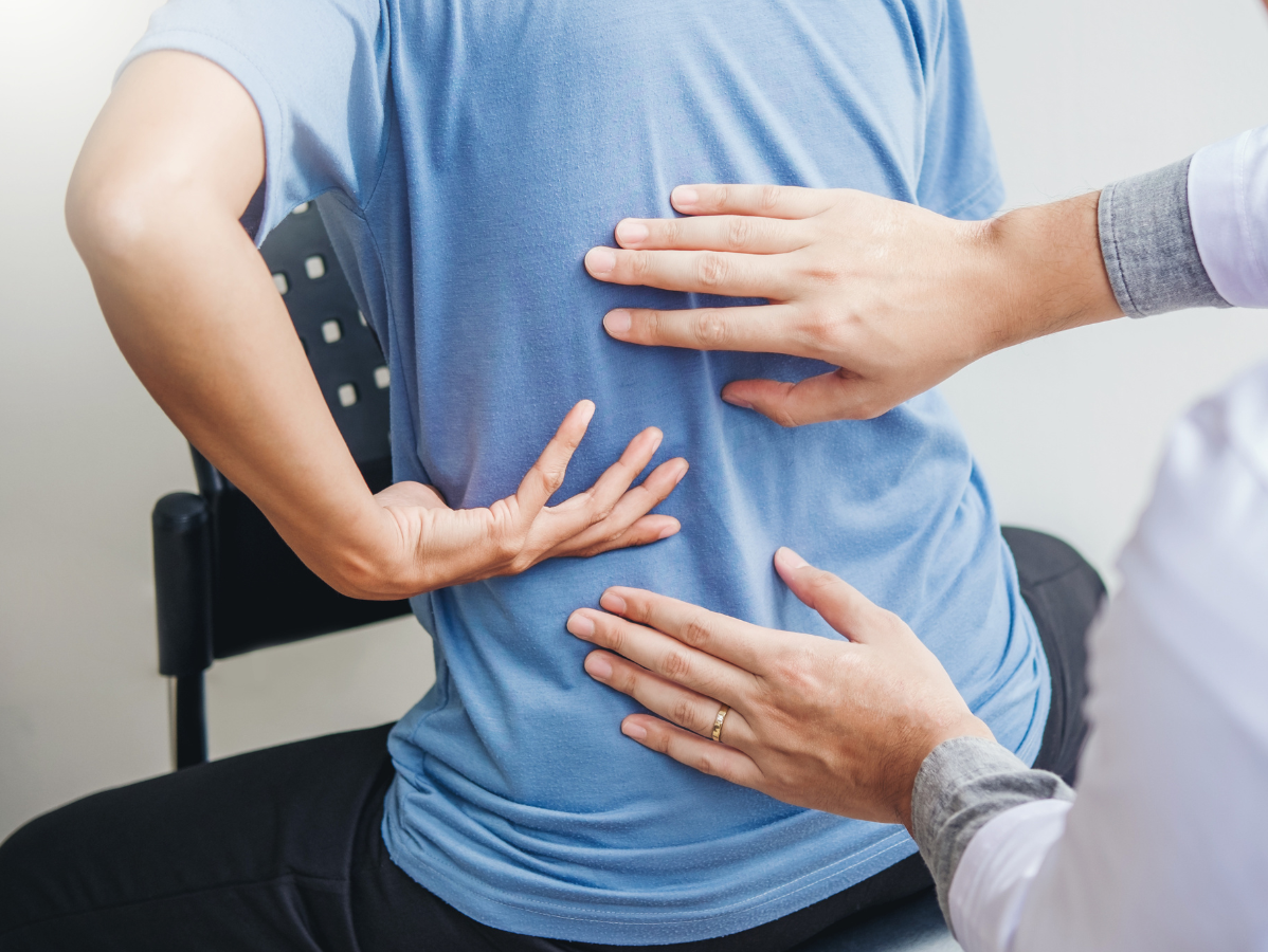 Doctor examining a patient's back. The patient wears blue, while the doctor wears white. Indoors, sitting.