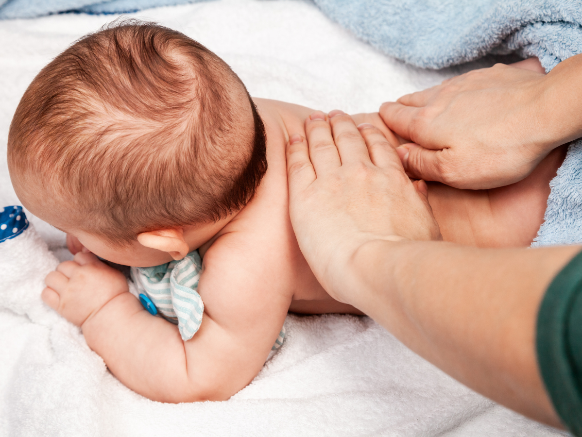 Baby lying on stomach, receiving a back massage with hands.