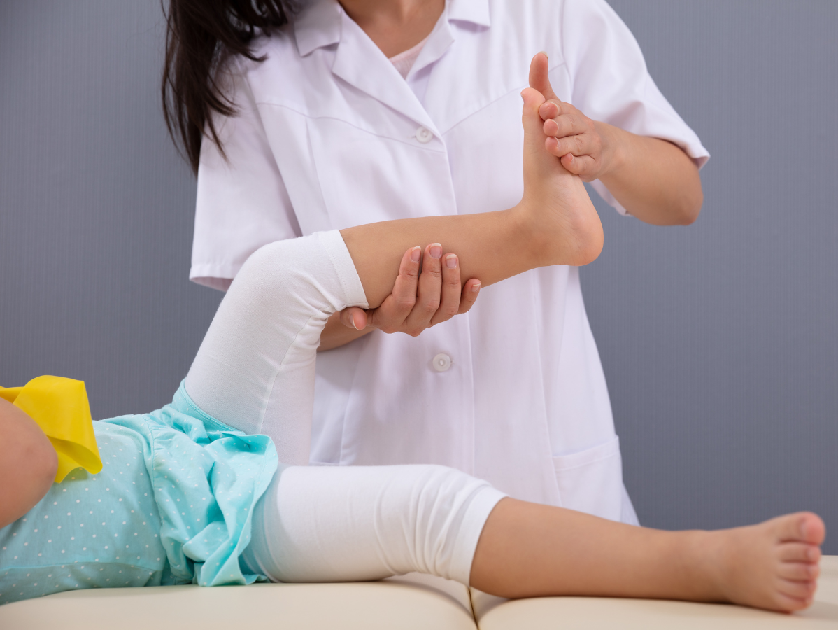 Therapist gently stretches a child's leg and foot on a therapy table.