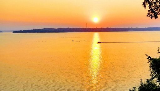 Golden sunset over a calm lake, sunlight reflecting on the water, with a boat and distant island.