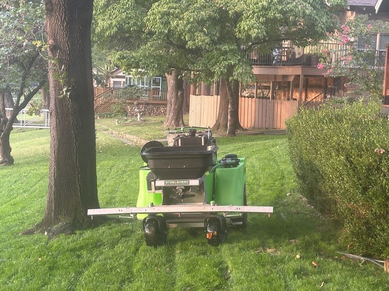 Lawn care machine spraying grass; green lawn, trees, house in background.