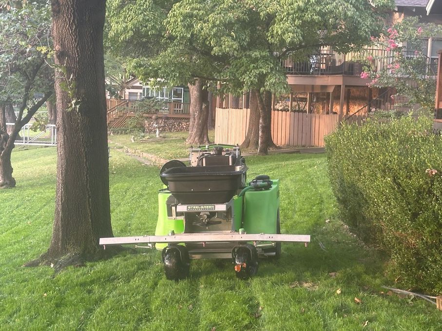 Lawn sprayer on a grassy yard, spraying a lawn near trees. Green and black machine, sunny day.