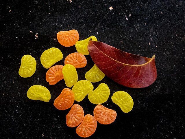 A pile of orange and yellow candy next to a red leaf.