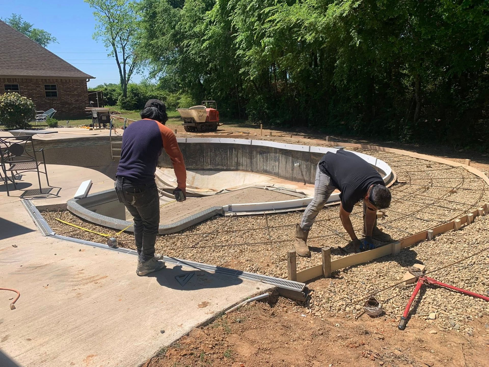 Two men are working on a swimming pool in a backyard.