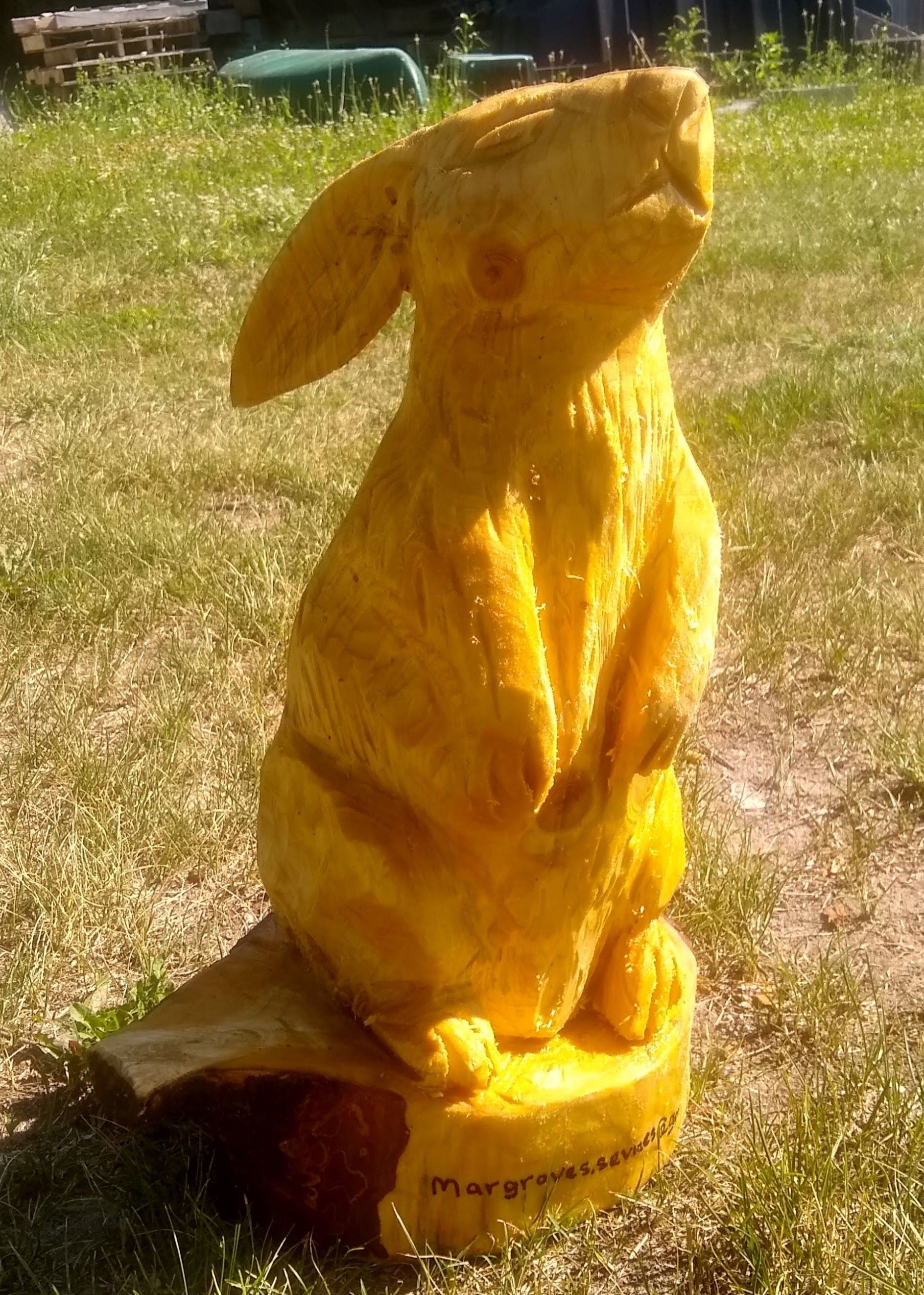 Yellow cat sculpture outdoors on a patchy grassy lawn, sitting upright in sunlight