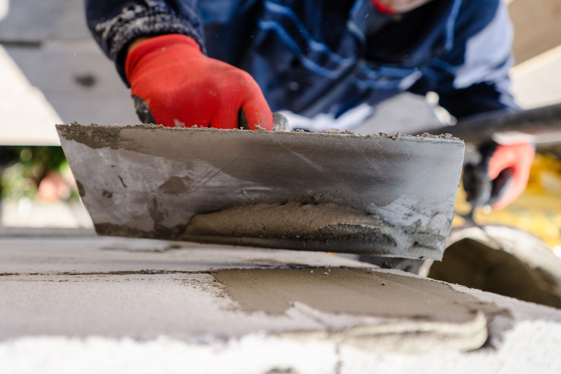 A construction worker plastering a wall outdoors with trowel cement mortar. He is holding a tool.