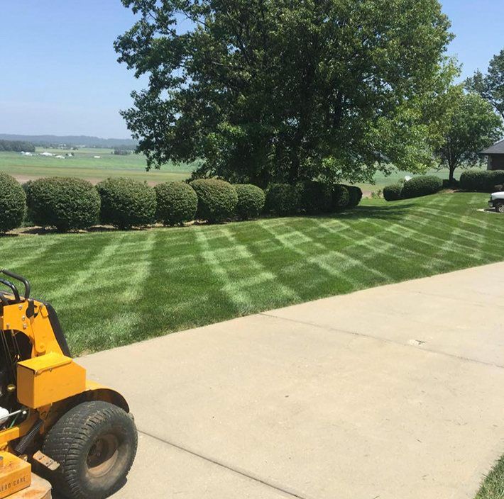 A yellow lawn mower is parked on a sidewalk next to a lush green lawn.
