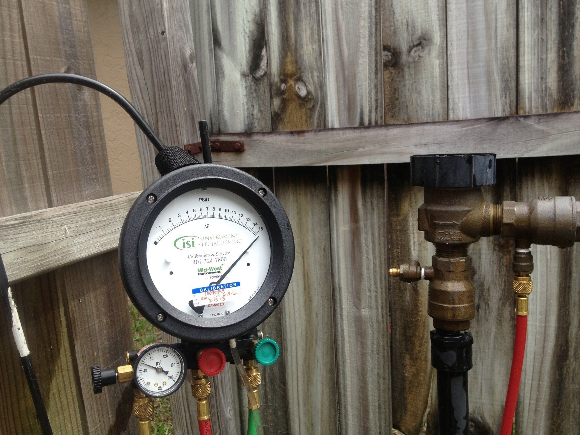 A pressure gauge is sitting next to a wooden fence.