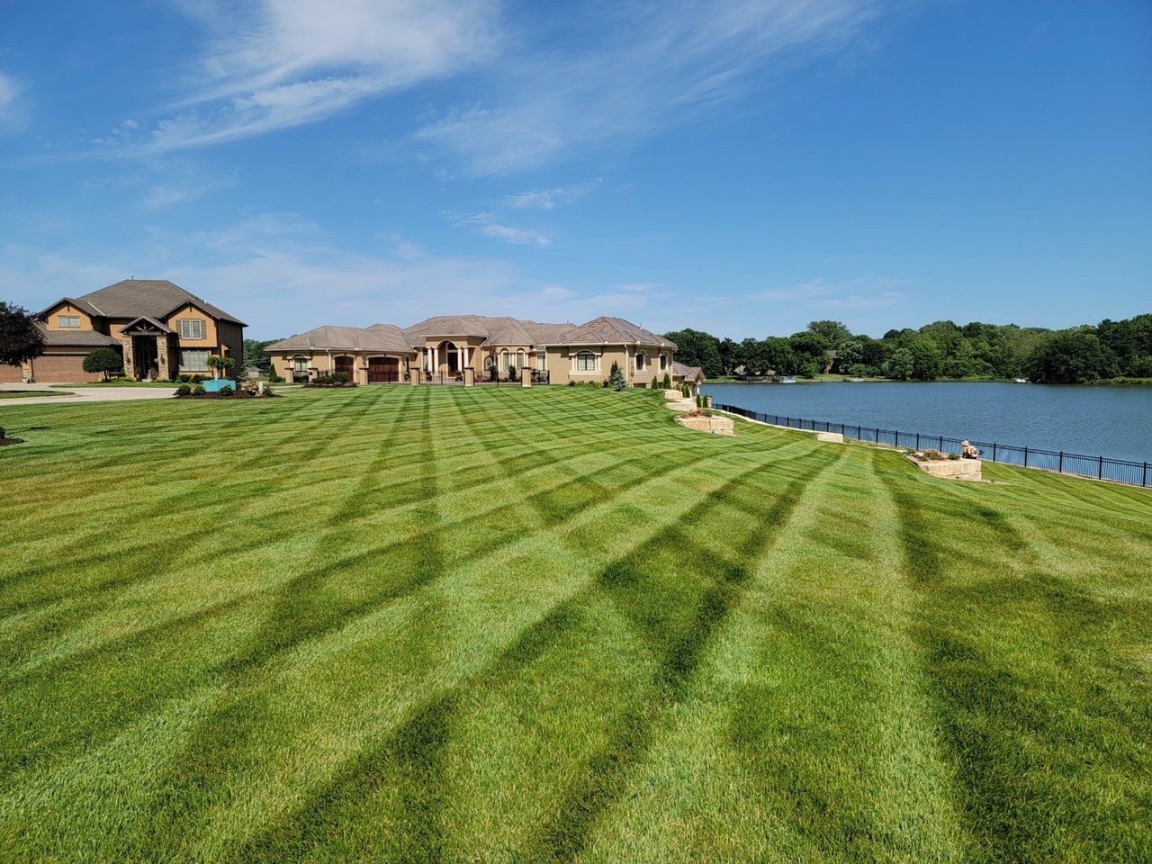 A large lawn with a house in the background and a lake in the background.