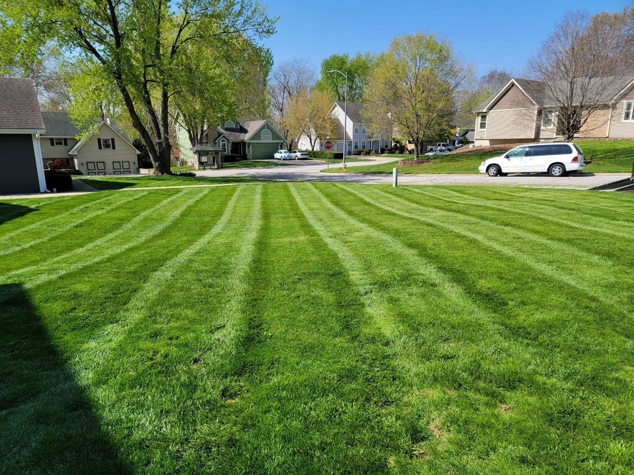 A white van is parked in front of a lush green lawn.