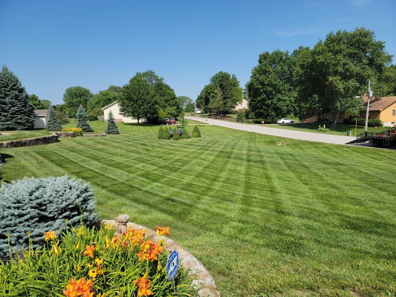A lush green lawn with flowers in the foreground and a road in the background.