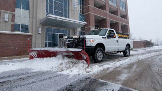A white truck is plowing snow in front of a building.
