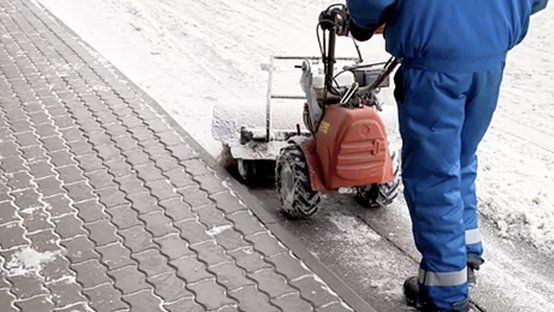 A man is using a snow blower to clean the sidewalk.