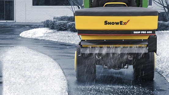 A snow spreader is spreading snow on a driveway