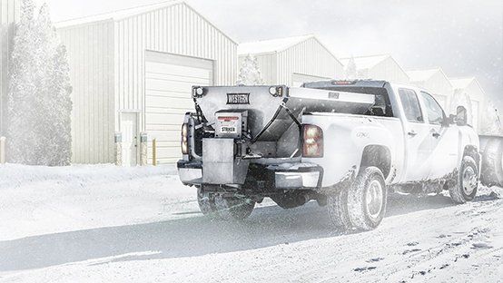 A white truck with a snow plow attached to the back is parked in the snow.