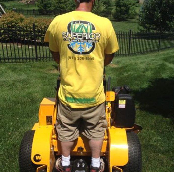 A man wearing a yellow superior shirt is riding a yellow lawn mower