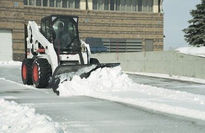 A bobcat snow plow is clearing snow from a parking lot.