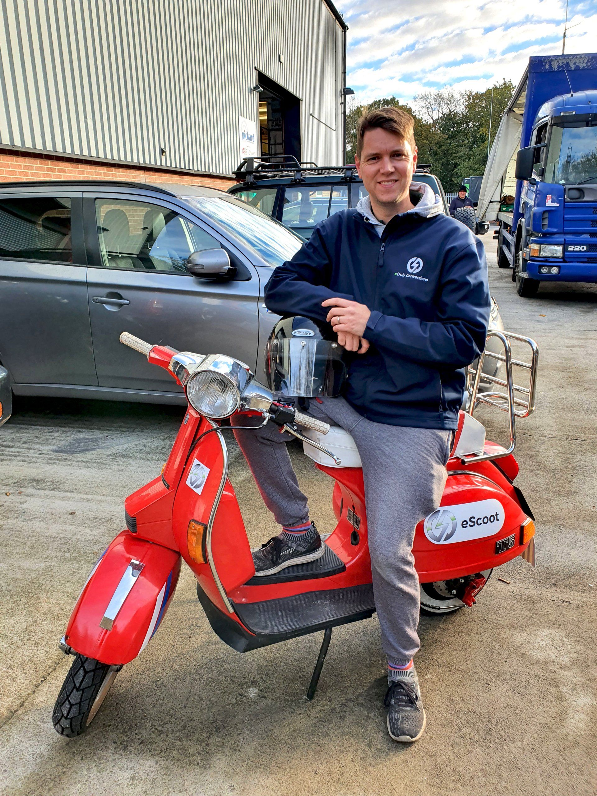 A young man is sitting on a red scooter in a parking lot.