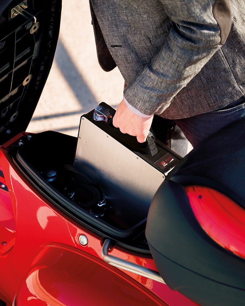 A man is loading a battery into the trunk of a red motorcycle