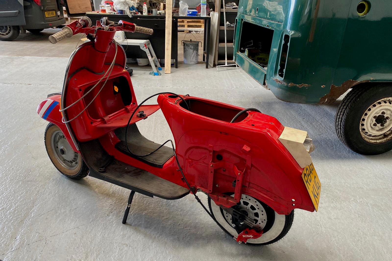 A red scooter is parked in a garage next to a green van.
