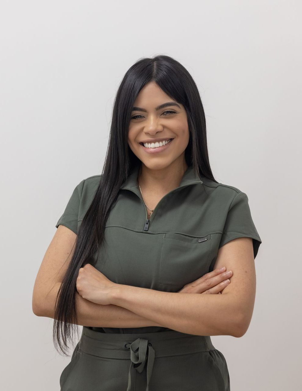 A woman in a green jumpsuit is smiling with her arms crossed.