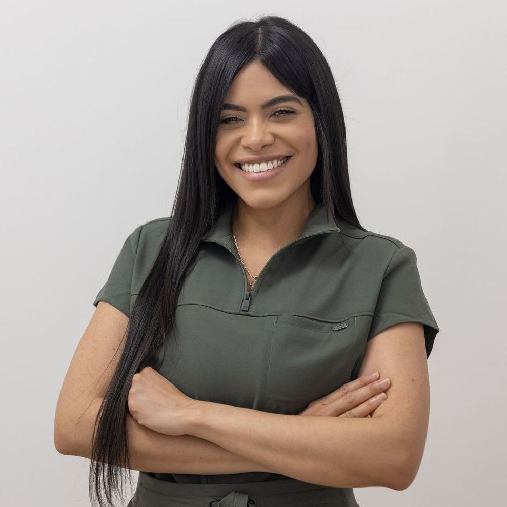 A woman in a green jumpsuit is smiling with her arms crossed.