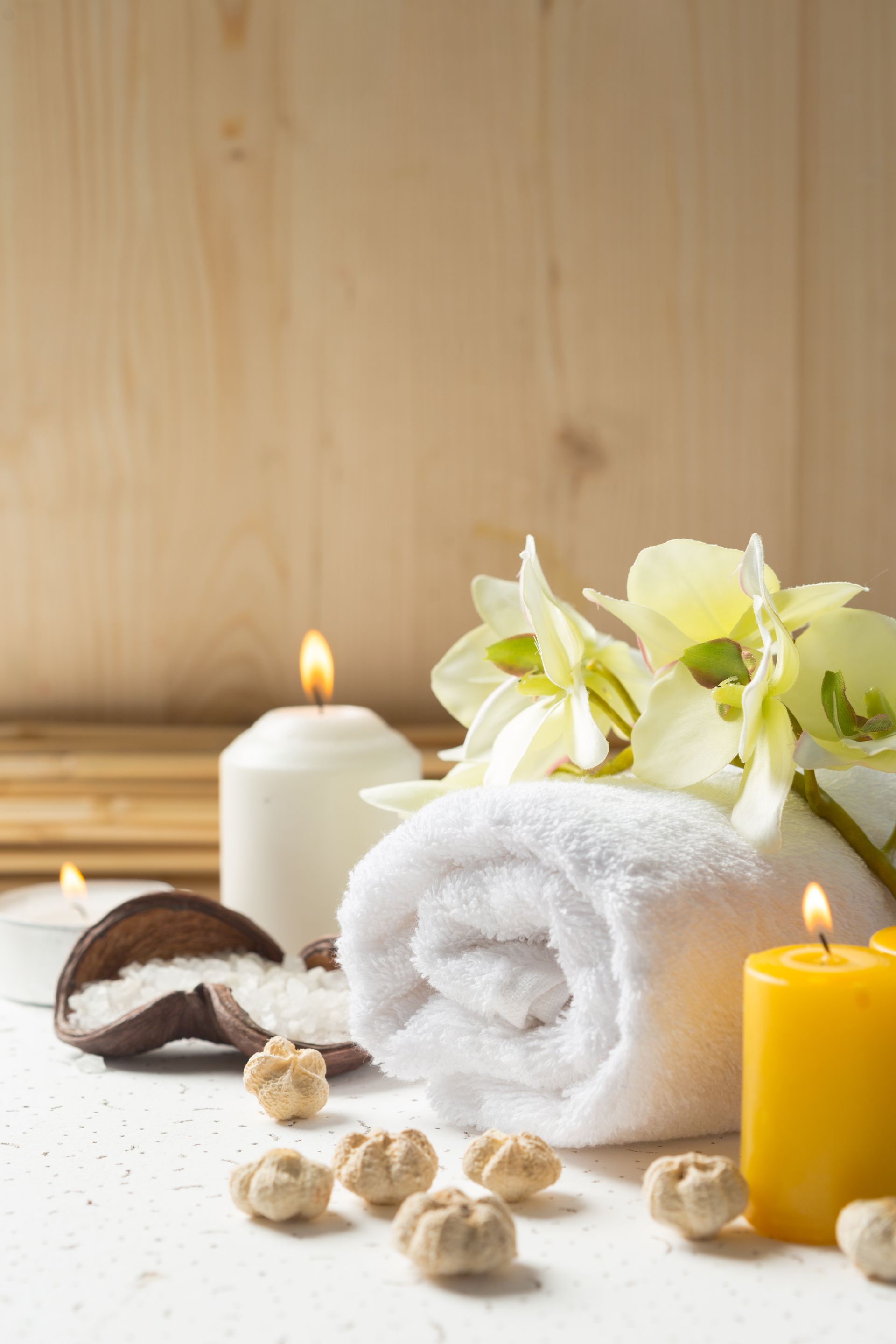 A rolled up towel , candles , flowers and sea salt on a table.
