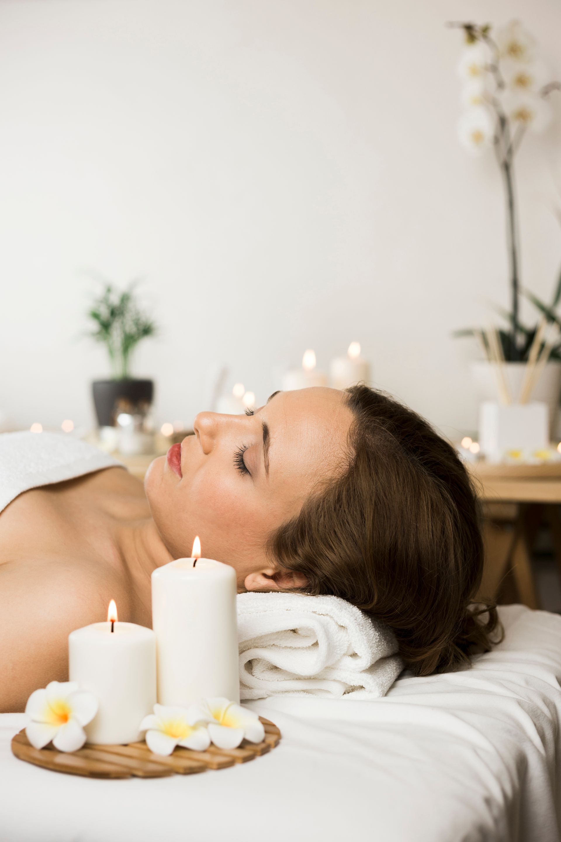A woman is laying on a massage table with candles and towels.