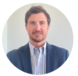 Man in a blue blazer and button-down shirt smiles, set against a plain background.