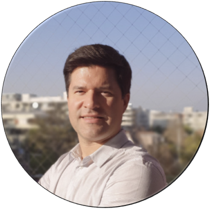 Man with short dark hair, smiling, wearing a light-colored shirt, outdoors with buildings in background.