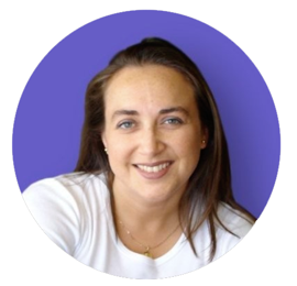 Woman smiling, wearing a white shirt, in front of a purple backdrop.