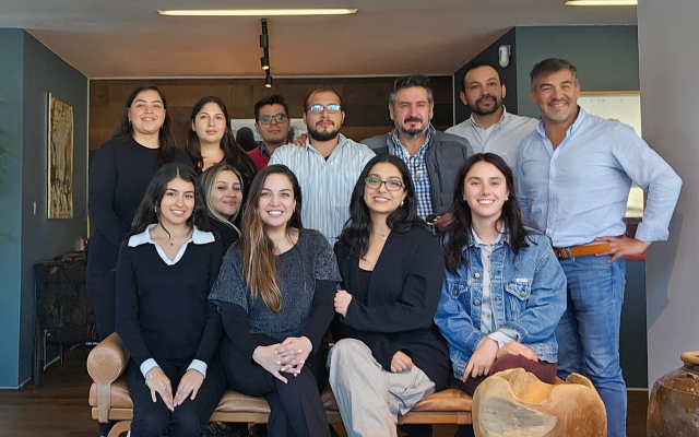 Retrato grupal de diez personas posando en una escalera interior, con sonrisas informales y una iluminación cálida.
