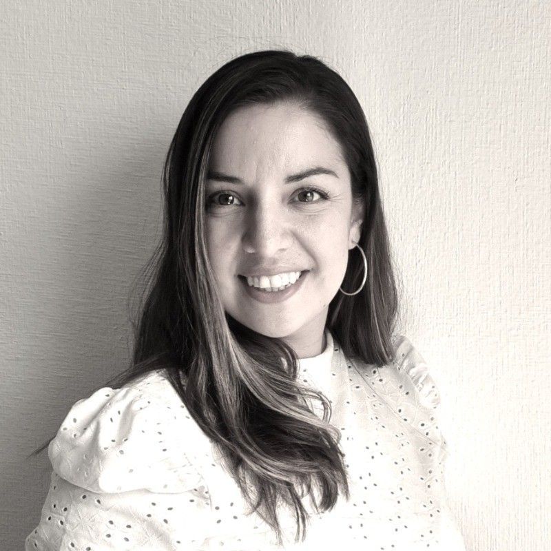 Mujer de cabello castaño, sonriente, vistiendo un blazer azul marino y un top color crema.