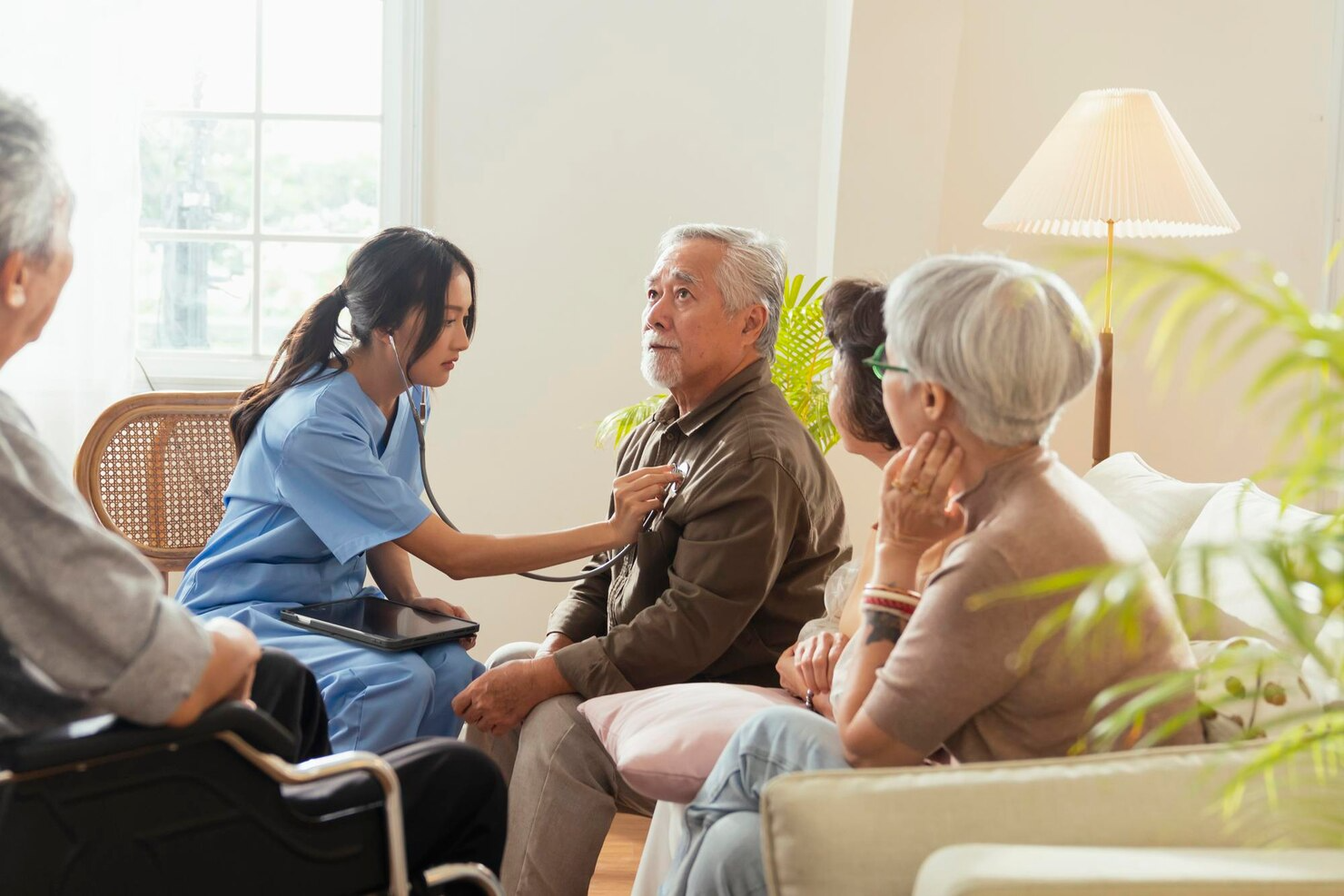 A nurse is listening to an elderly man 's heartbeat with a stethoscope.