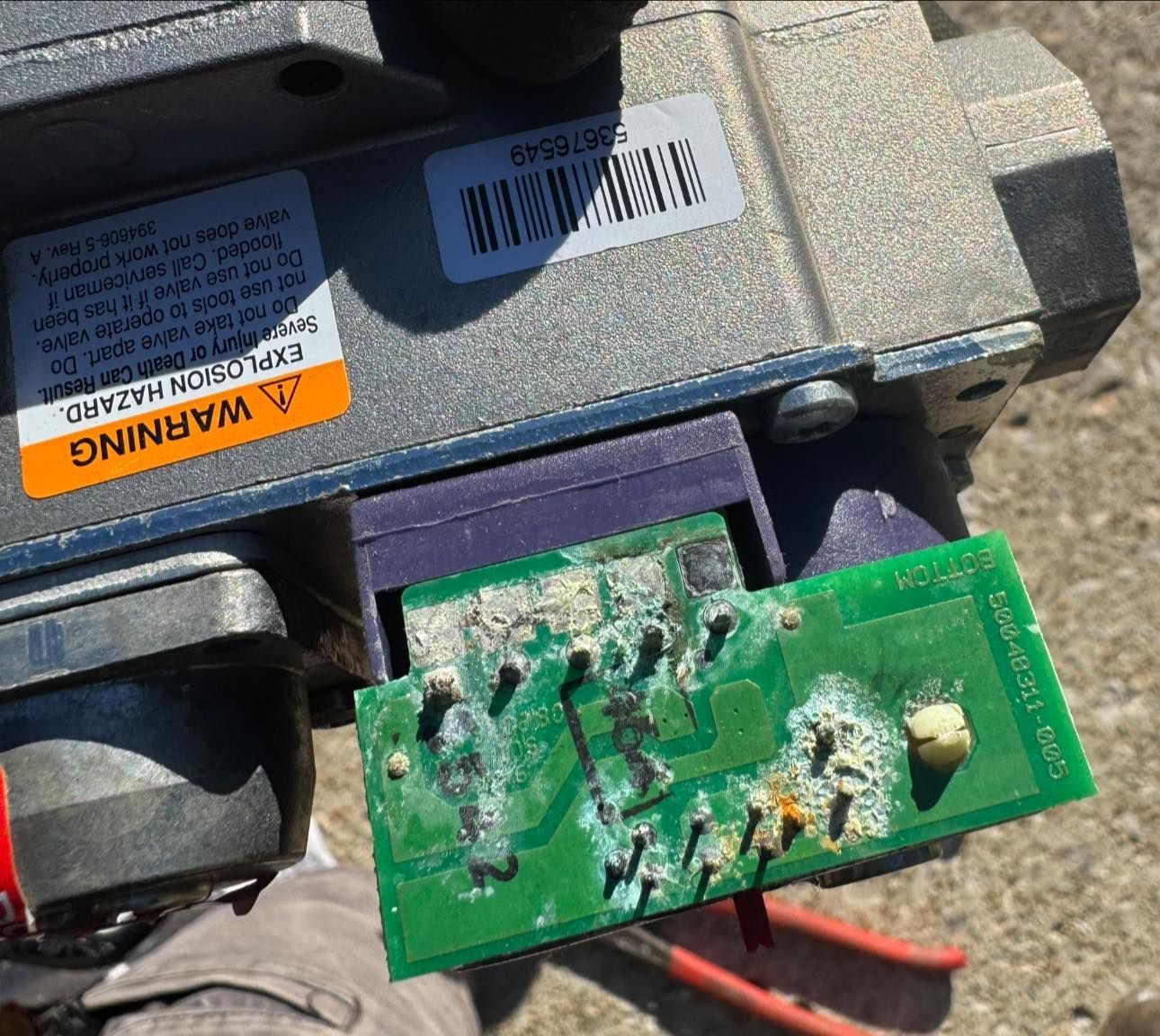A close-up view of a corroded green circuit board attached to a metal industrial valve component.