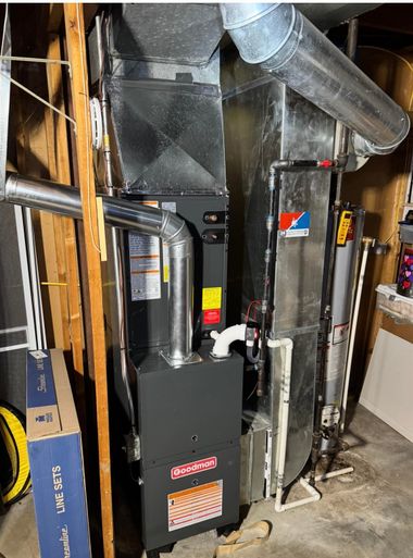 A tall, metal furnace unit and attached silver ductwork are positioned in a basement next to wooden support beams.