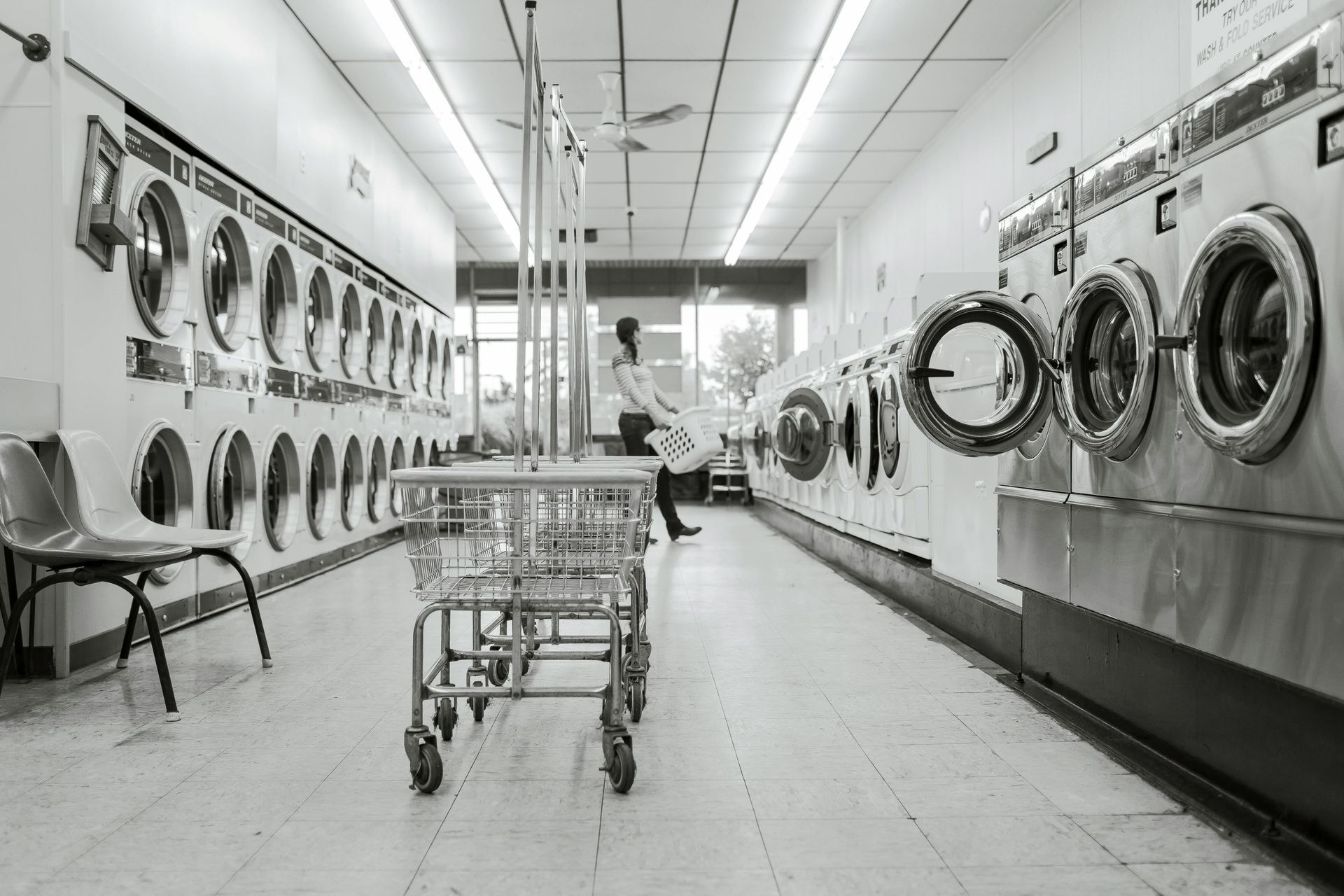 Laundry room with rows of washing machines. A person loads laundry into a machine.