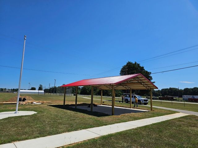A carport with a red roof is sitting in the middle of a grassy field.