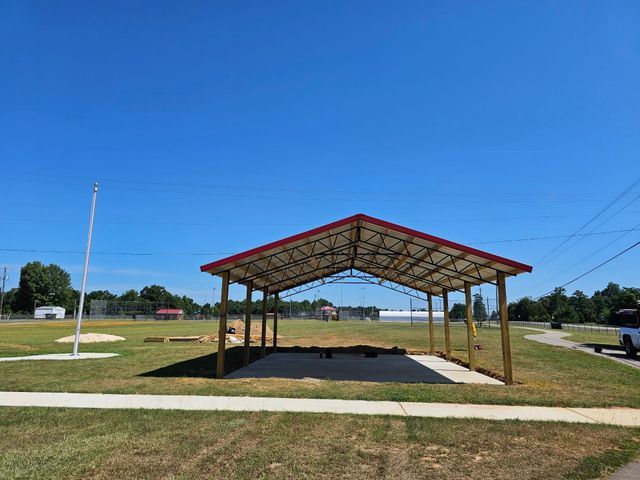 A wooden pavilion with a red roof is sitting in the middle of a grassy field.