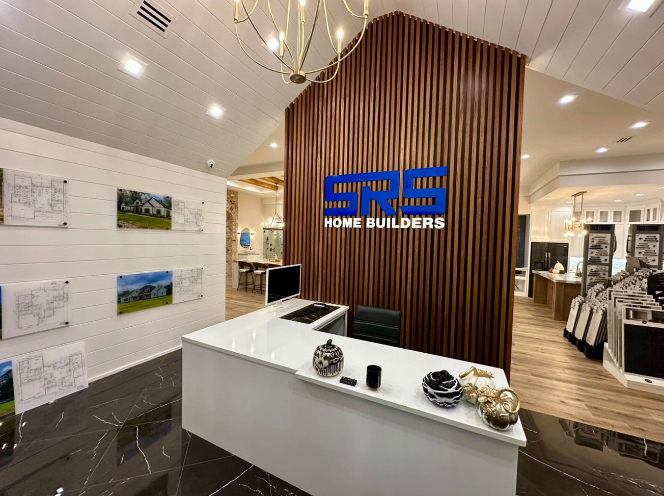 Reception area of a home builder, with a white countertop desk and logo against a wooden slat wall.