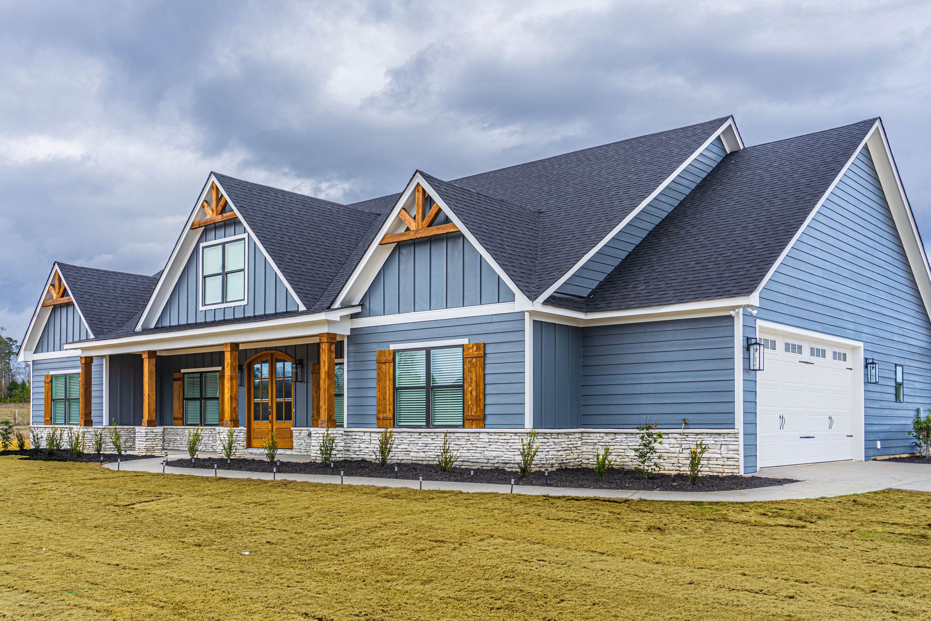 A large blue house with a black roof is sitting on top of a lush green field.