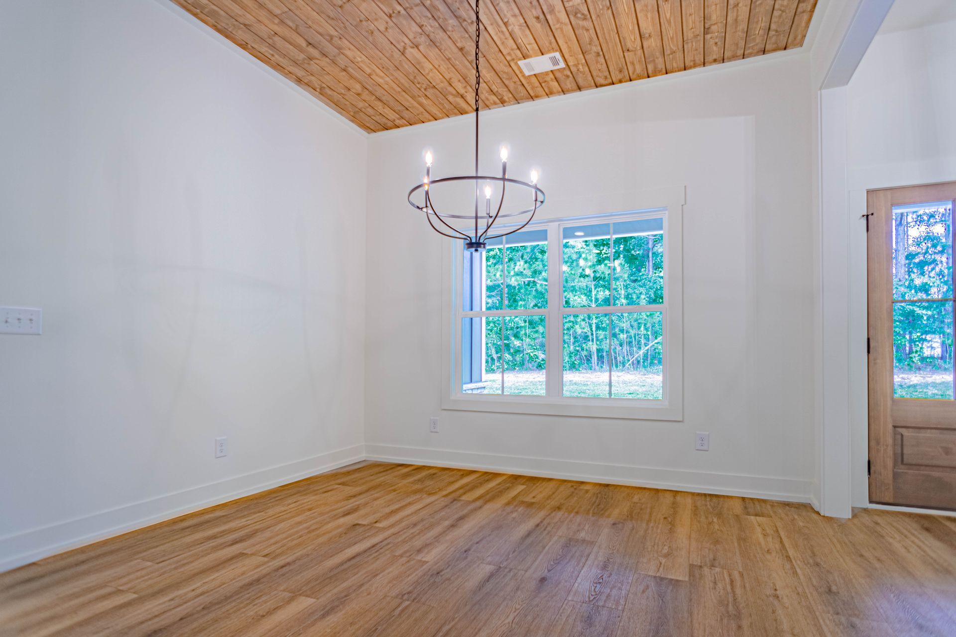 An empty room with hardwood floors and a chandelier hanging from the ceiling.
