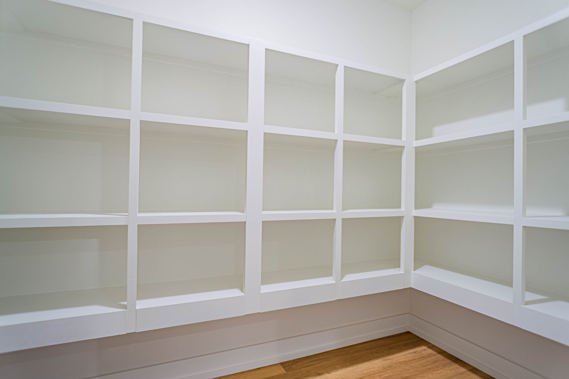 An empty pantry with lots of shelves and a wooden floor.