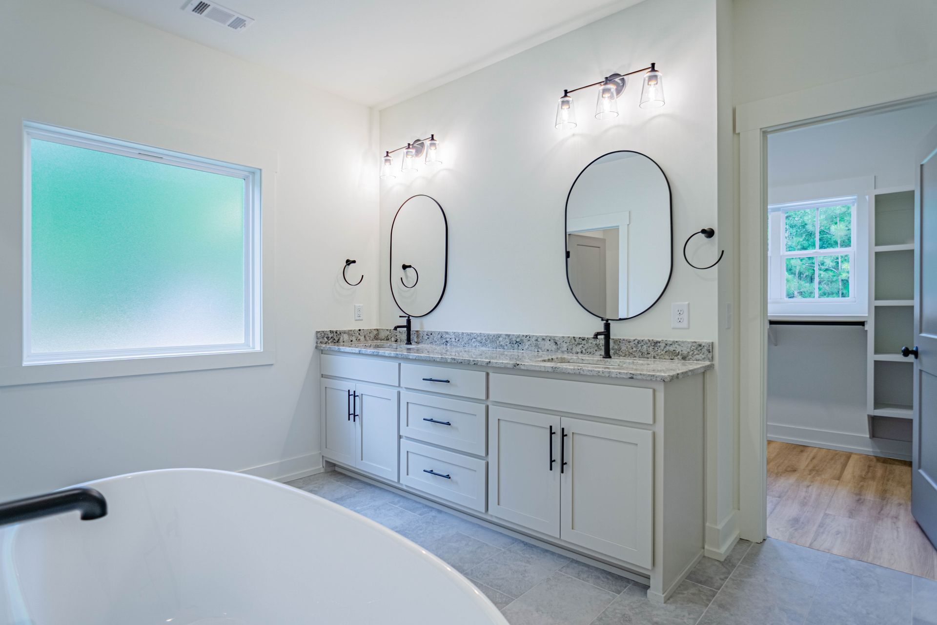 A bathroom with two sinks , two mirrors and a bathtub.