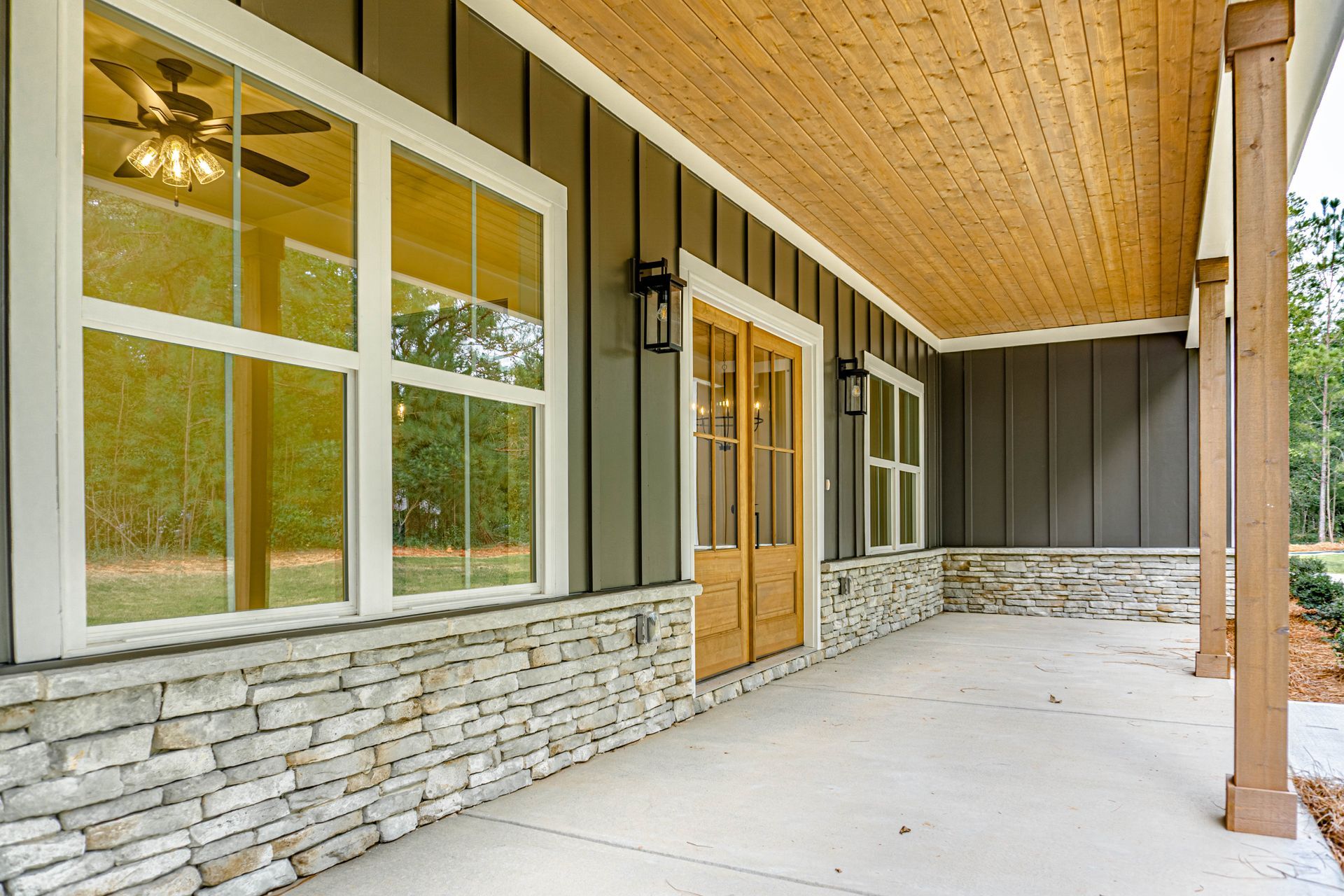 A porch with a ceiling fan and a lot of windows on a house.