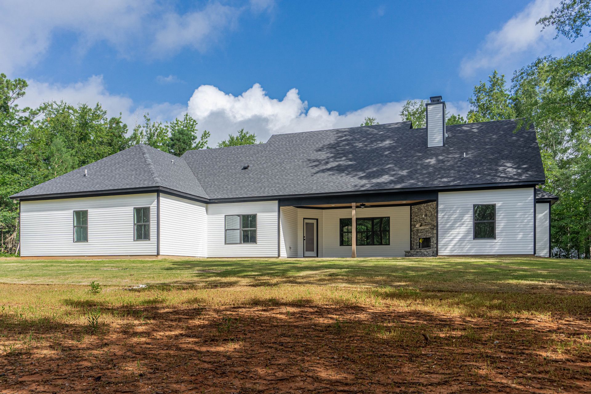 A white house with a black roof is sitting on top of a lush green field.