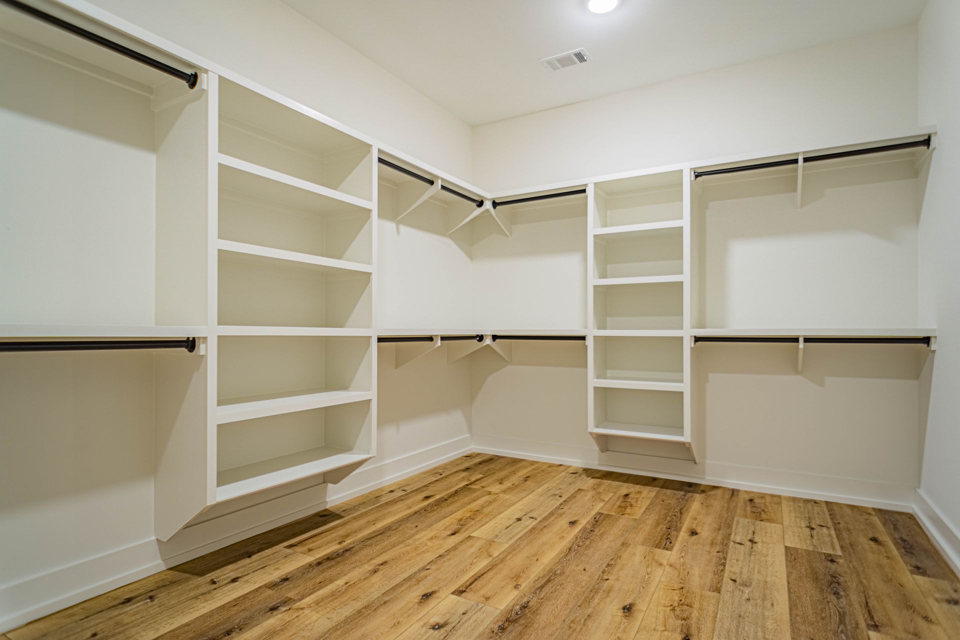 A walk in closet with wooden floors and white shelves.