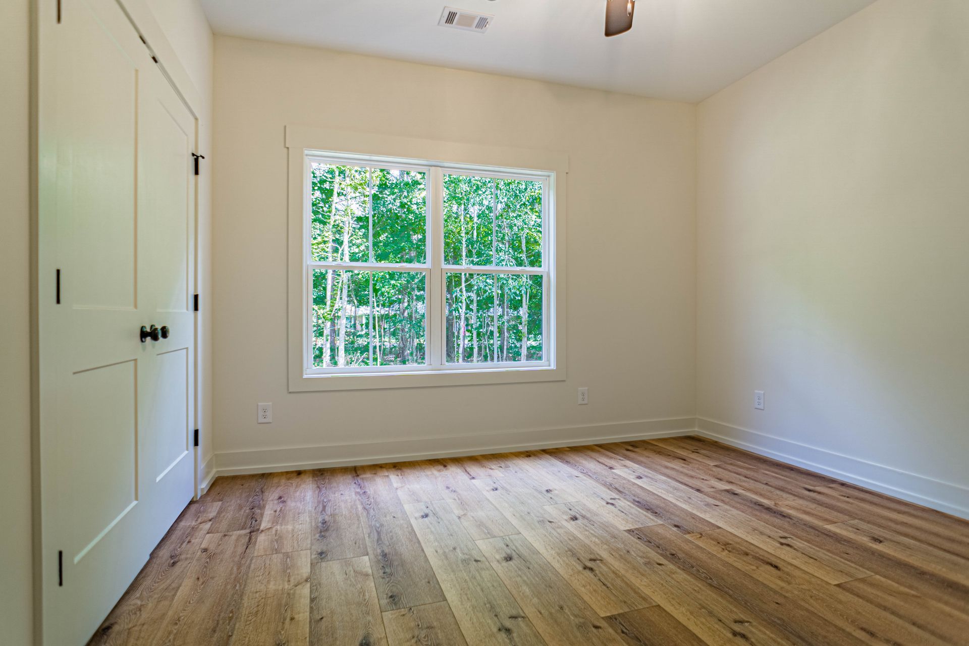 An empty bedroom with hardwood floors and two windows.